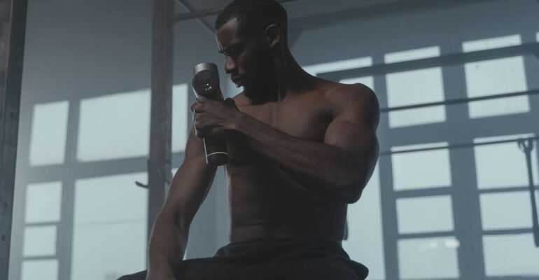 Man using a handheld massage gun on his upper arm in a gym