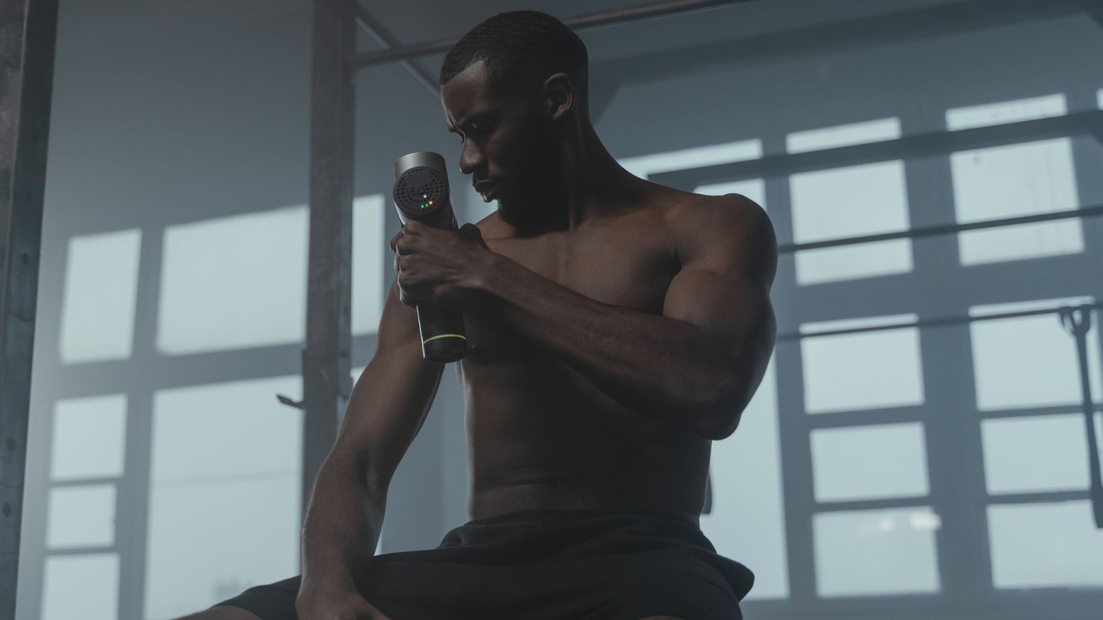 Man using a handheld massage gun on his upper arm in a gym